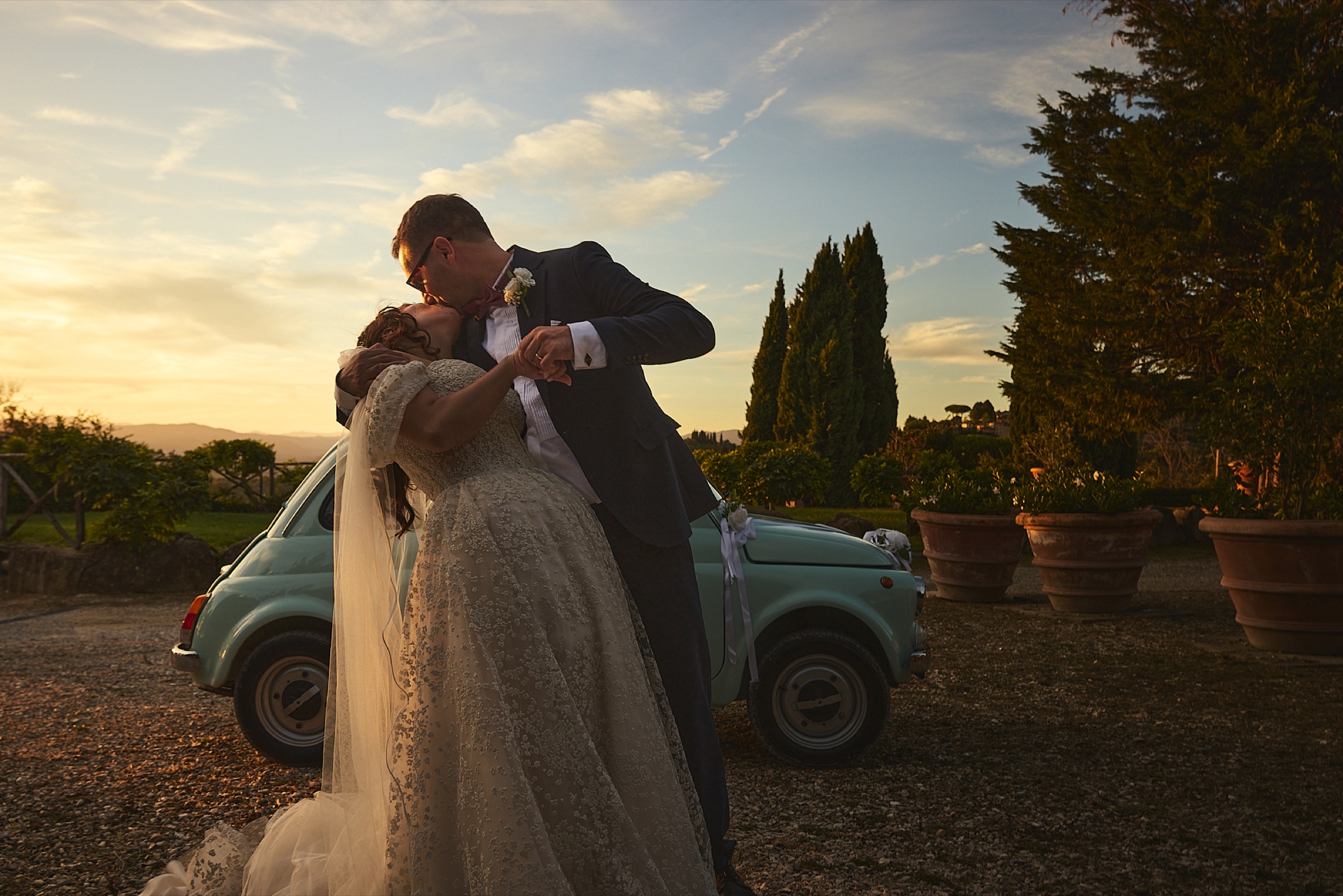 Gli sposi accanto a un'auto d'epoca al tramonto